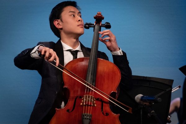 Young man playing cello with expressive look on his face.