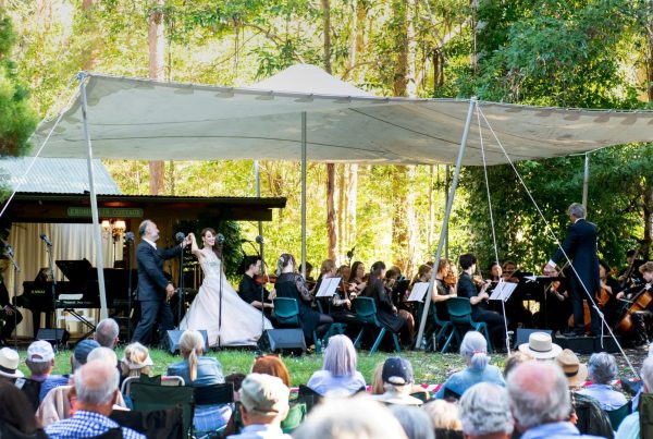 Man and woman dancing next to orchestra in an outdoor setting with trees.