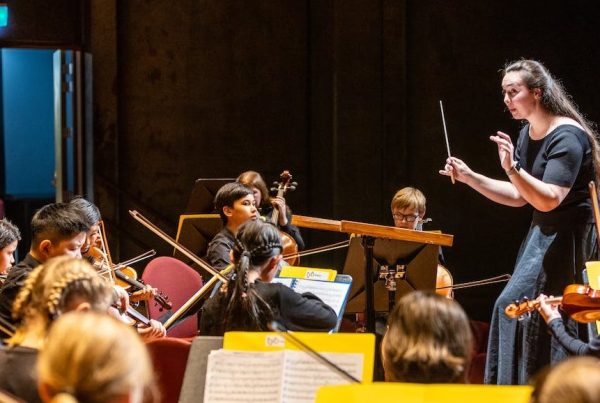 Children playing in an orchestra with a female conductor